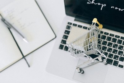 Laptop mit geöffnetem Onlineshop neben Notizblock und Kaffeetasse